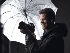 Photographe souriant utilisant un parapluie blanc lors d'une séance photo